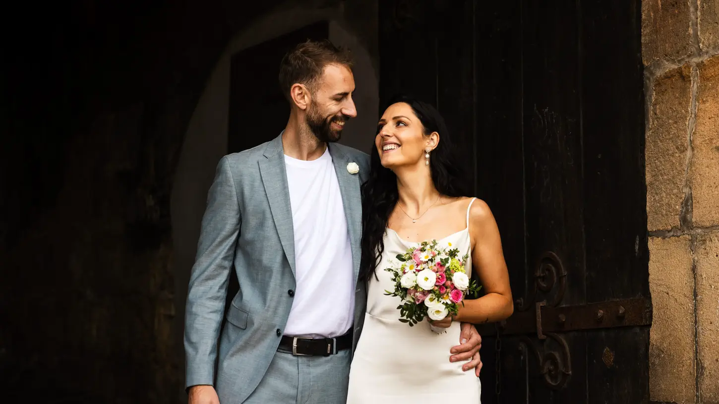 Hochzeitsfotos vor einer dunklen Wand mit einem lachenden Ehepaar