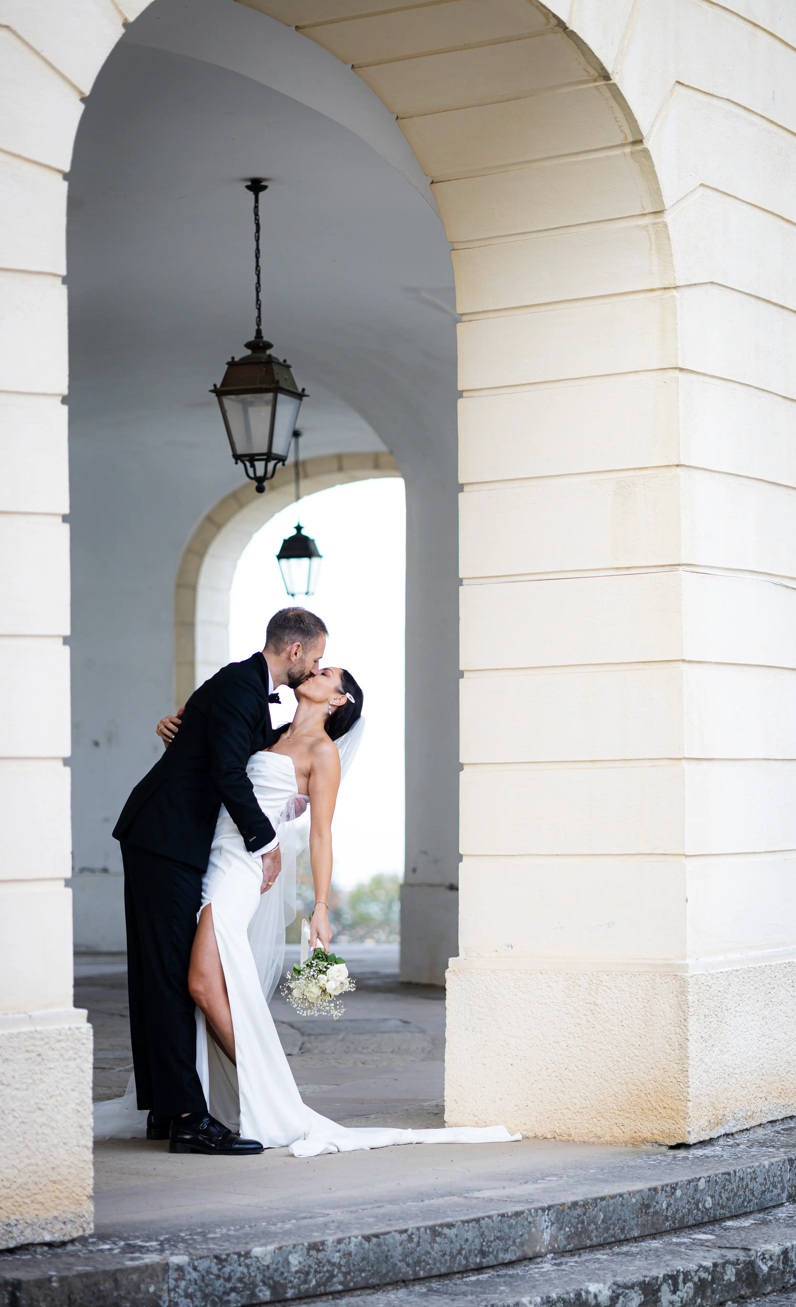 Hochzeitfotos bei einem Schloss in einem Torbogen. Die Braut lässt sich küssen und nach hinten fallen.