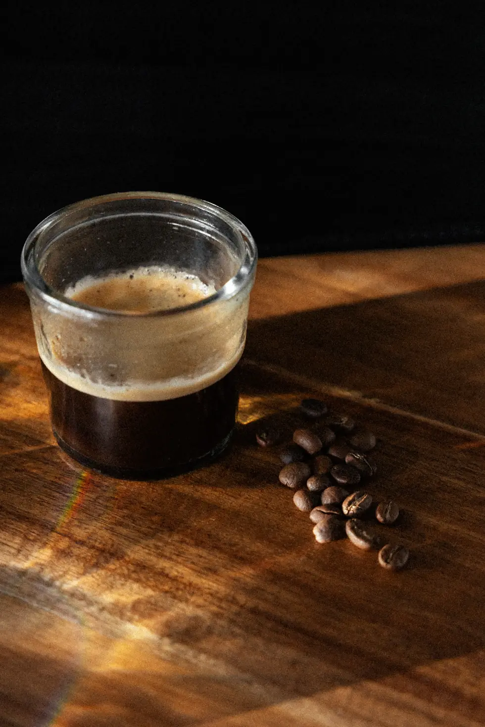 Das Produkt Kaffee wurde bei dieser Produktfotografie ins Licht gerückt. Man sieht Kaffee in einem Glas mit Bohnen daneben.