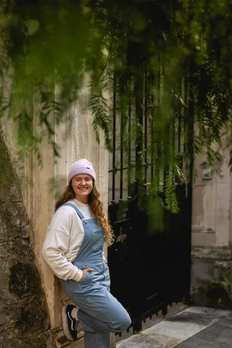 Junge Frau lehnt sich mit Latzhose für das Portrait an die Hauswand. 