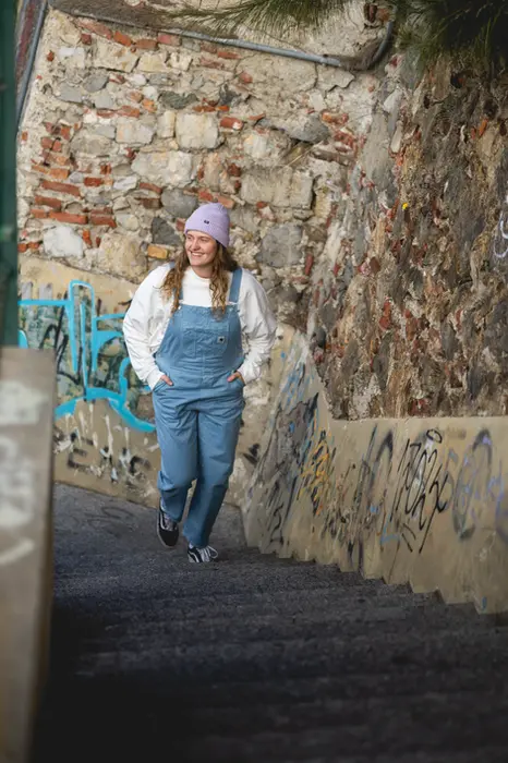 Portrait bei dem eine junge Frau Treppen hochläuft und eine Latzhose trägt. 