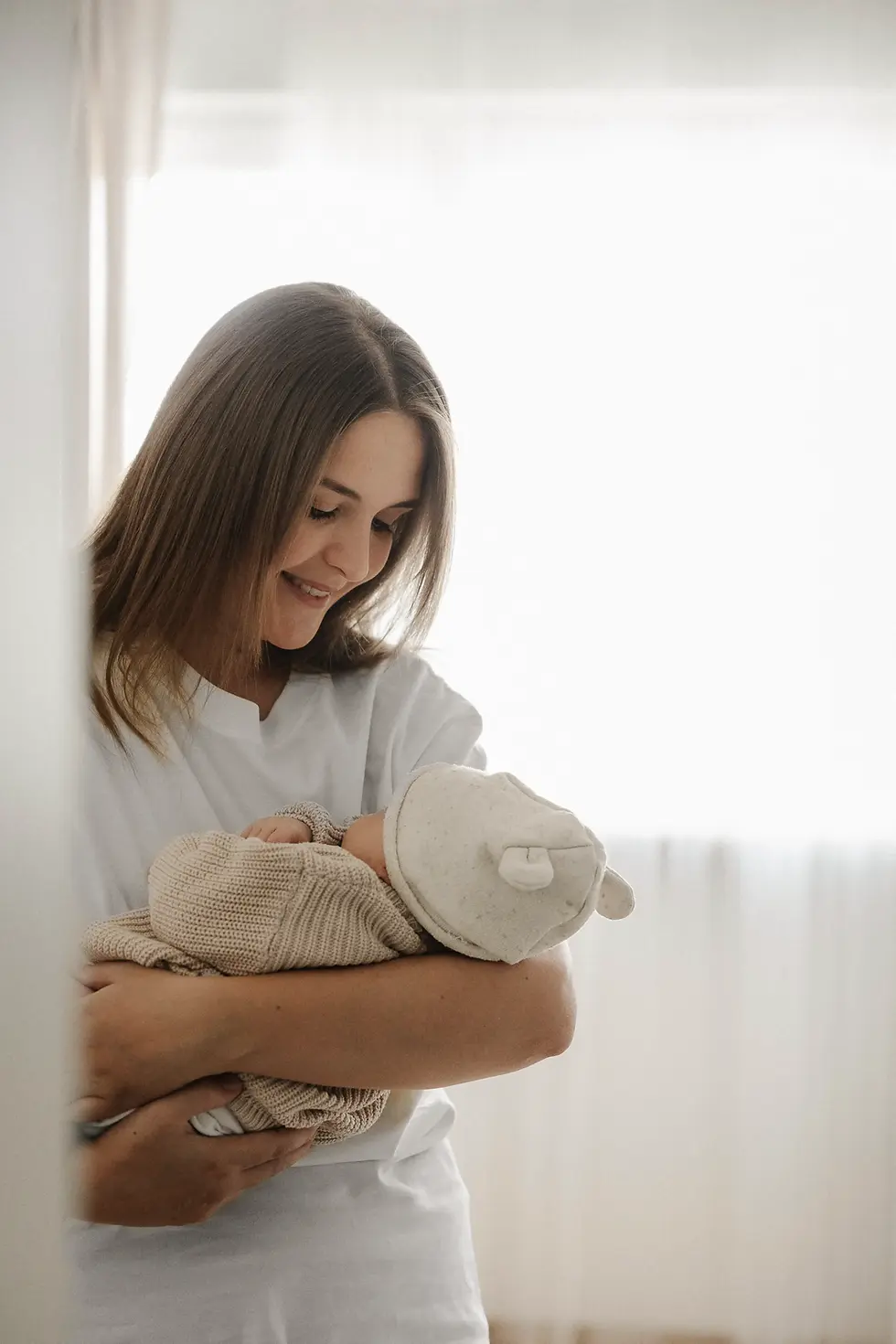 Newborn Shooting von einer Mama, die in einem Zimmer steht und ihr Baby im Arm hält. Man sieht leicht den Türrahmen verschwommen.