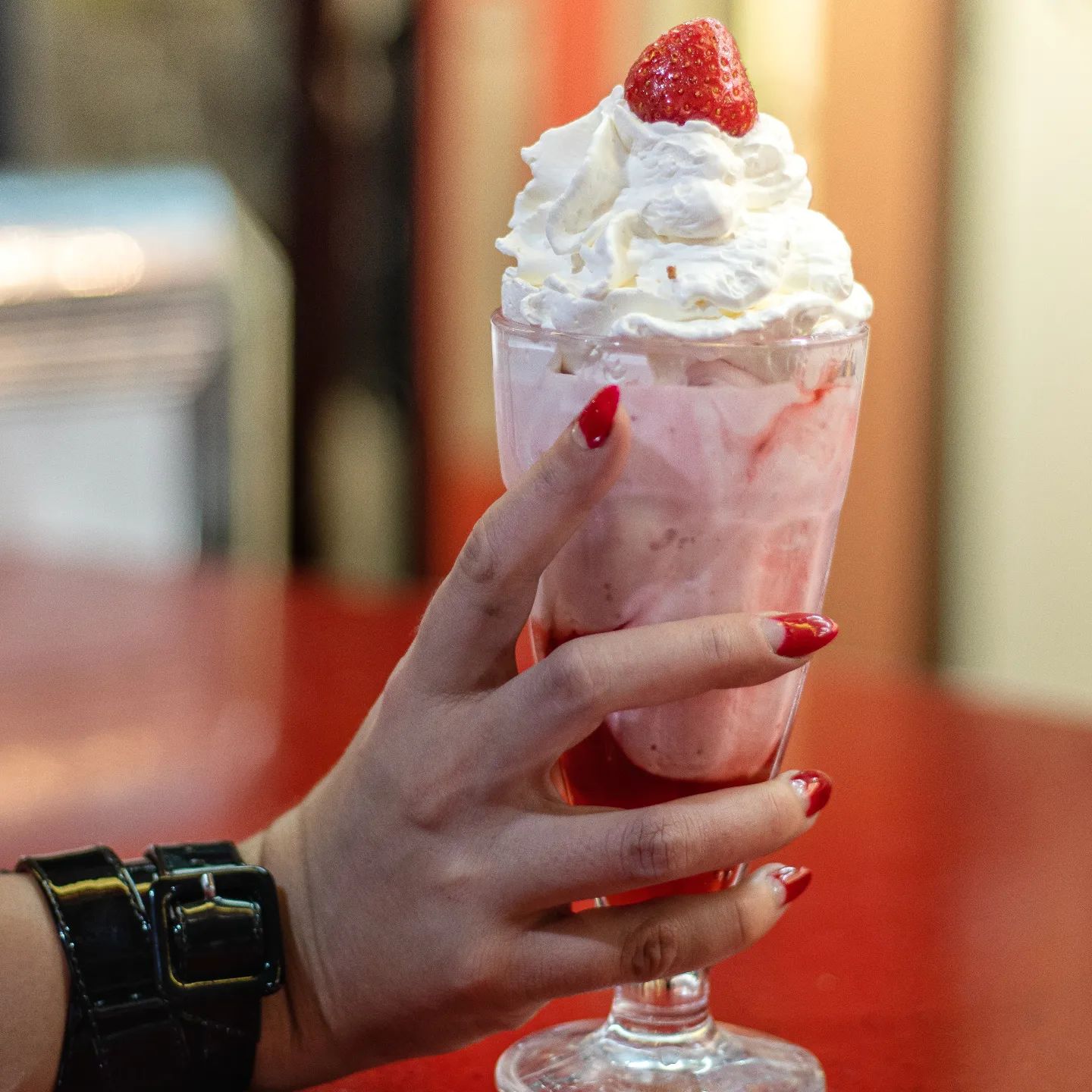 Indulgence in a glass! A lady holds a delicious strawberry milkshake at the bar, ready to dive into creamy sweetness.
