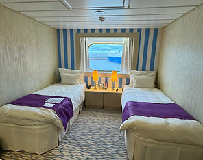 Twin bed configuration with bedside tables, lamps, phone and a picture window in an outside cabin on Ambassador Ambition.