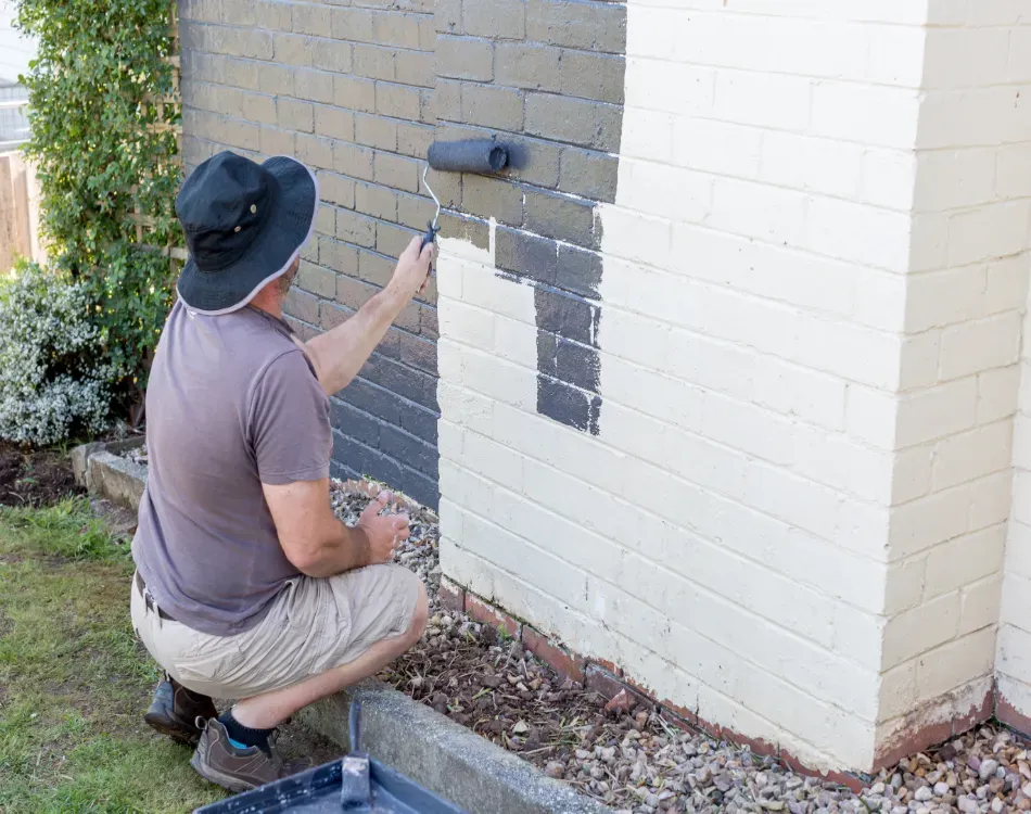 A man painting the brick exterior of a house.