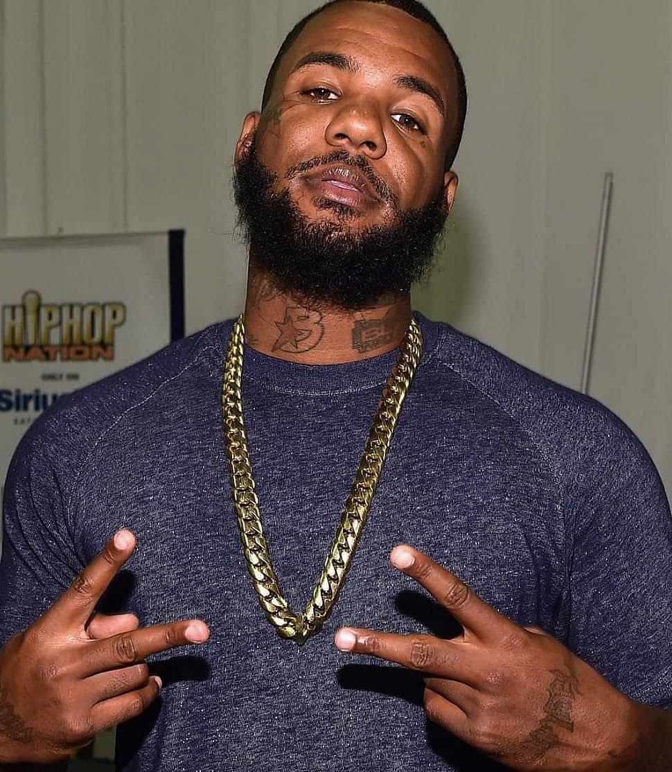 Das Bild zeigt Rapper The Game mit einem blauem T-Shirt und einer Goldkette um den Hals. Mit den Händen zeigt der Rapper jeweils das "Peace-Zeichen"