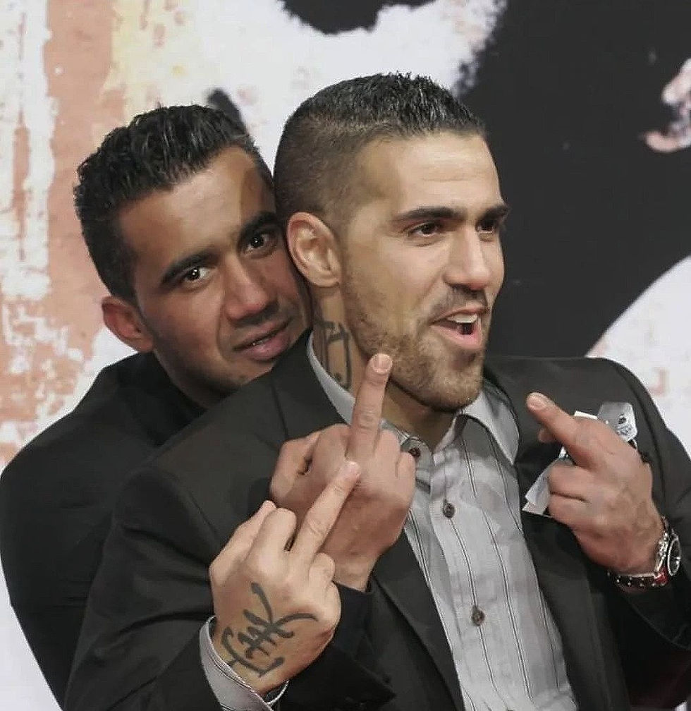 Das Bild zeigt links den Clan-Chef Arafat Abou-Chaker mit schwarzen Anzug. Er umarmt von hinten den Rapper Bushido. Er trägt auch einen schwarzen Blazer mit einem grauen Hemd. Beide zeigen die Mittelfinger vor dem Körper.