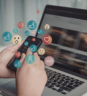 A person holding a smartphone whilst looking at a laptop - emojis coming out of the phone