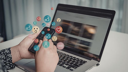 A person holding a smartphone in front of an open laptop. Several emojis are coming from the phone which signal listening online and digital engagement