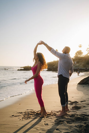 A white male twirling a female dressed in pink at the beach