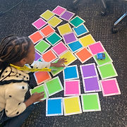 A joyful young girl engrossed in play, arranging vibrant squares on the floor with a smile on her face.
