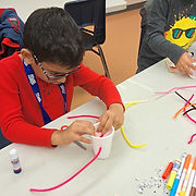Two kids happily crafting at a table, using colorful materials to create their imaginative masterpieces.