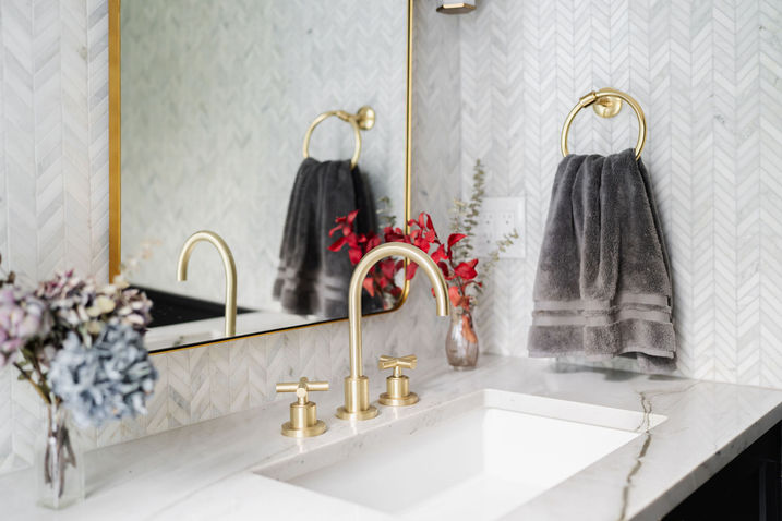 Bathroom vanity with dual sinks, gold fixtures, and decorative mirror
