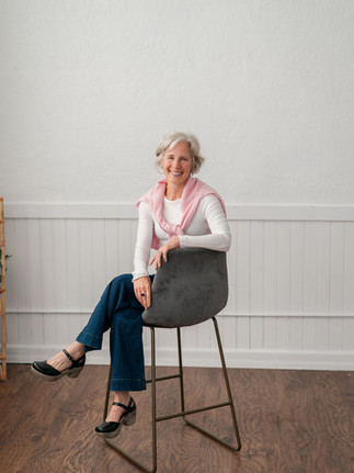 A wellness coach sitting on a still with a pink cardigan around her shoulders