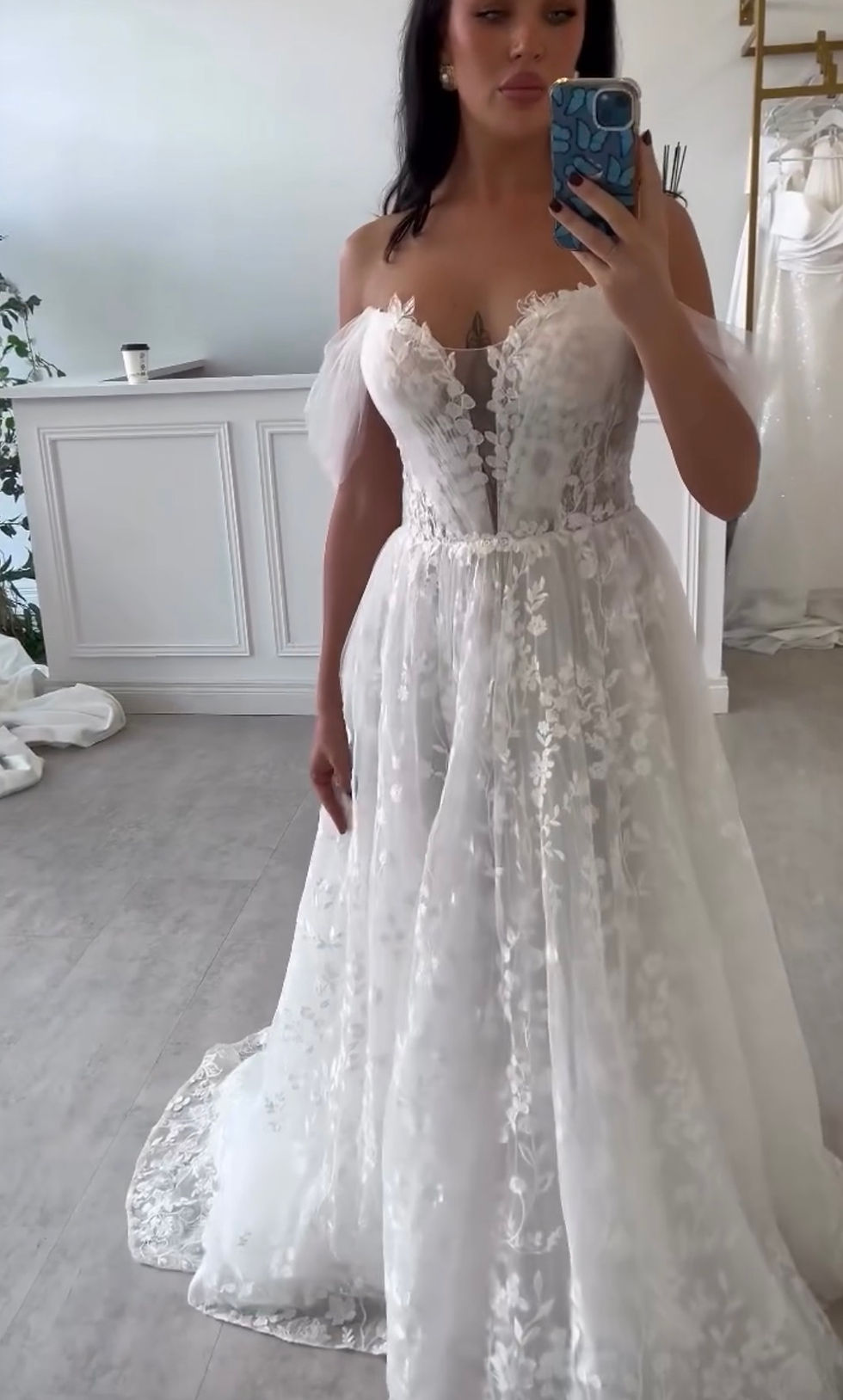 Woman wearing an off-shoulder white wedding dress, Chosen by Khya, Orelle. Elegant bridal gown.