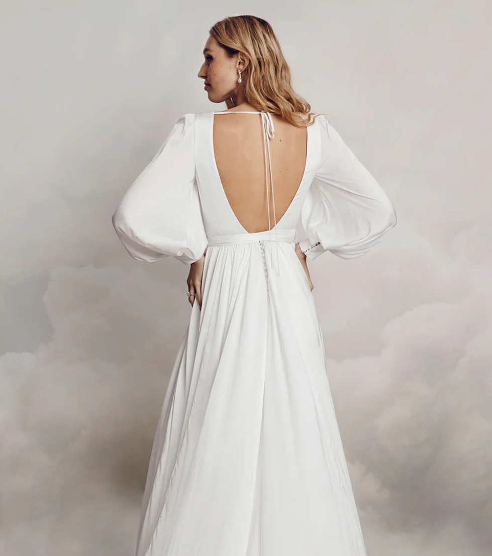 Woman wearing a white wedding dress with open back posing in studio.