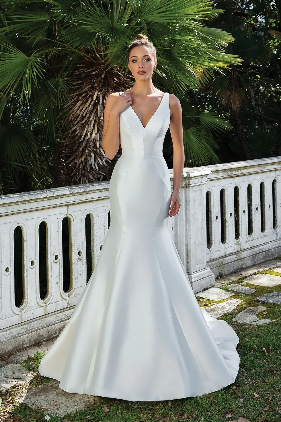 Bride in elegant V-neck white mermaid wedding dress in garden.