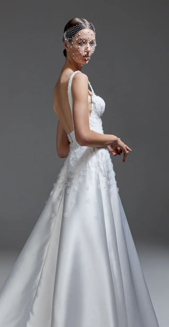 Woman in white wedding dress with open back and floral appliqués.