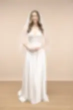 Smiling woman wearing a wedding dress and veil stands in a studio setting.