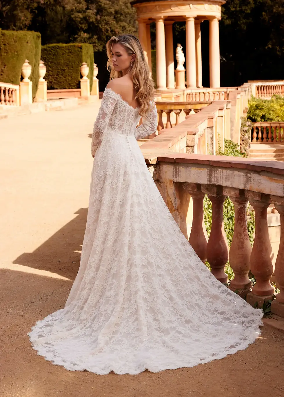 Woman in elegant off-shoulder white lace wedding dress standing on balcony. And She loves bridal boutique in berkshire 