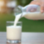 A glass of milk being poured with a green in the background