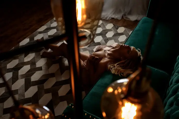 Boudoir portrait of a woman reclining on a green velvet couch, photographed through warm glowing light bulbs, creating a cinematic and intimate atmosphere.