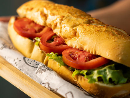 A fresh sub sandwich with lettuce and tomato on a wooden tray