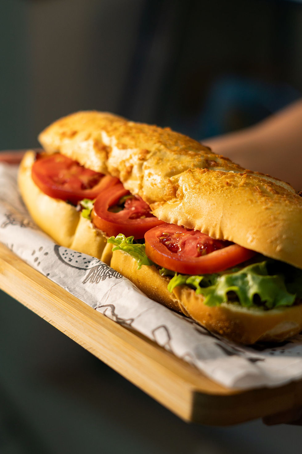 A fresh sub sandwich with lettuce and tomato on a wooden tray