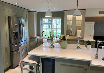 Anna Clare Bespoke shaker kitchen in Knebworth with soft green cabinetry, glass dresser and central island with quartz worktop