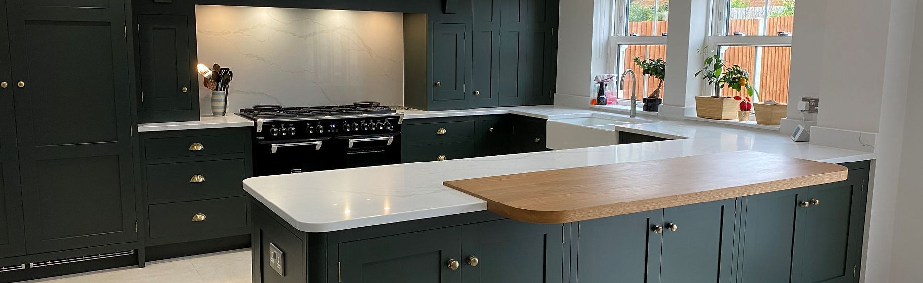 Bespoke dark green shaker kitchen with oak breakfast bar, range cooker, and classic tiled flooring