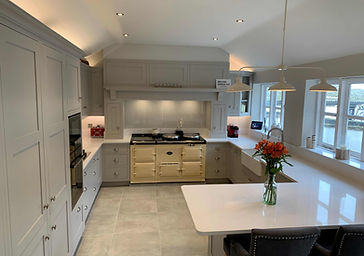 Bespoke kitchen with classic in-frame cabinetry and a cream AGA cooker, framed by soft grey units and under-cabinet lighting in a vaulted ceiling space.