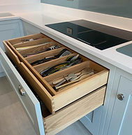 Bespoke two-tier oak cutlery drawer insert with layered compartments for utensils, shown open in a pale blue shaker kitchen.