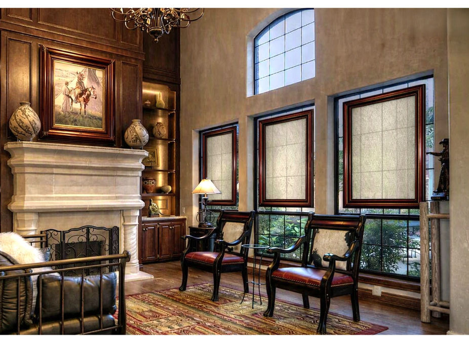 Mahogany‑framed SHAADS® window covers with Verona Beige light‑filtering fabric mounted on the upper portion of the window in a luxury estate living room, showing glass‑mounted installation with a thin edge of exposed glass for soft daylight and partial visibility.