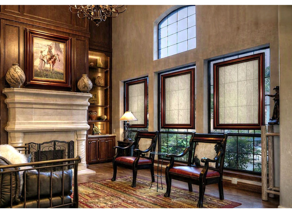 Mahogany‑framed SHAADS® window covers with Verona Beige light‑filtering fabric mounted on the upper portion of the window in a luxury estate living room, showing glass‑mounted installation with a thin edge of exposed glass for soft daylight and partial visibility.