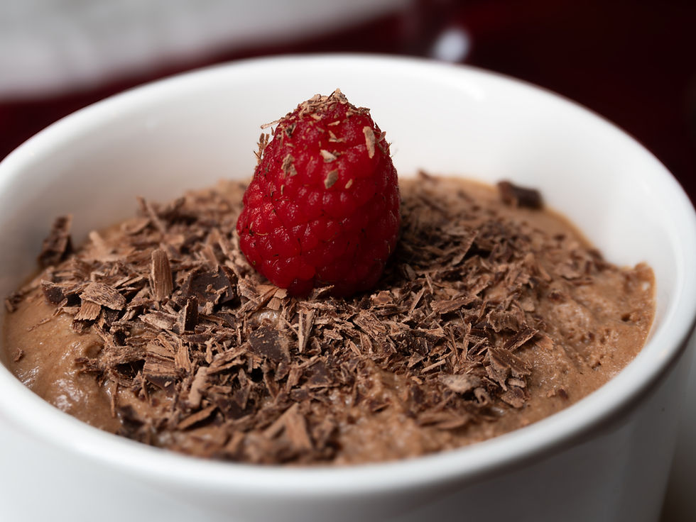 Chocolate mousse topped with a red raspberry and chocolate shavings in a white bowl.