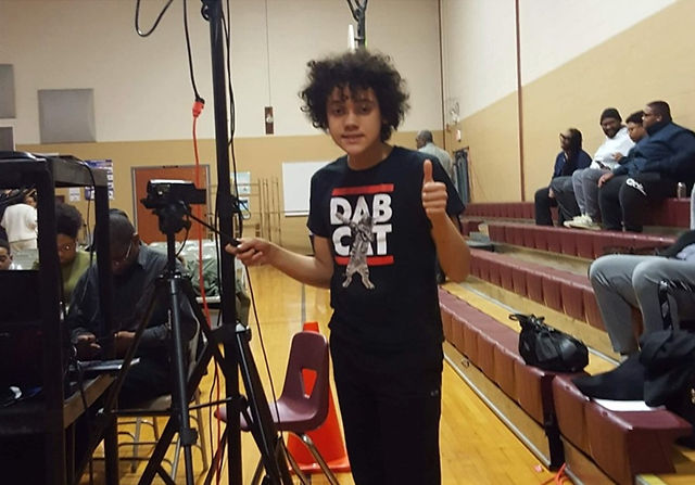 Young Solomon in a gymnasium operating a video camera on a stand