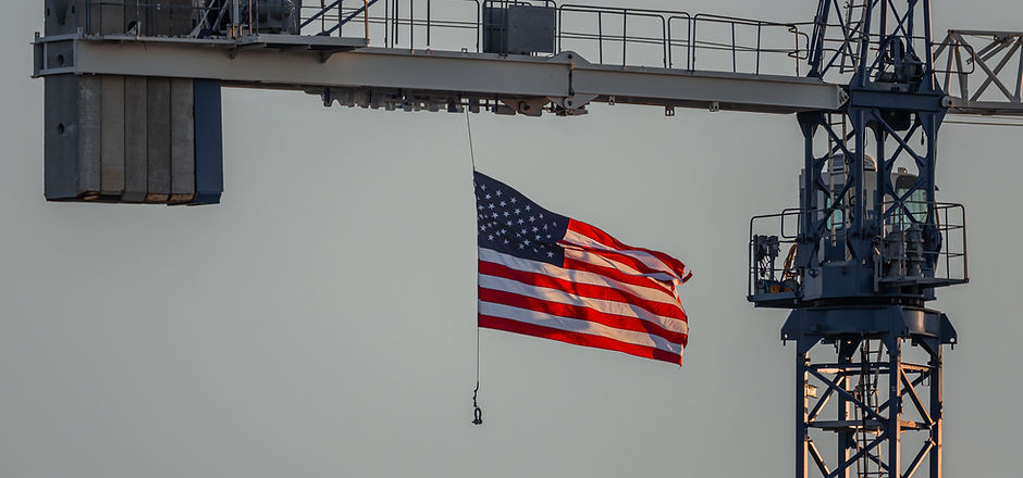 United States flag gracefully flying, back lit by setting sun and hanging from crane on a
