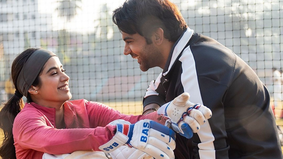 Man and woman smiling at each other in a cricket net area. The woman wears a pink top, the man a black jacket. Gloves have "BAS" text.
