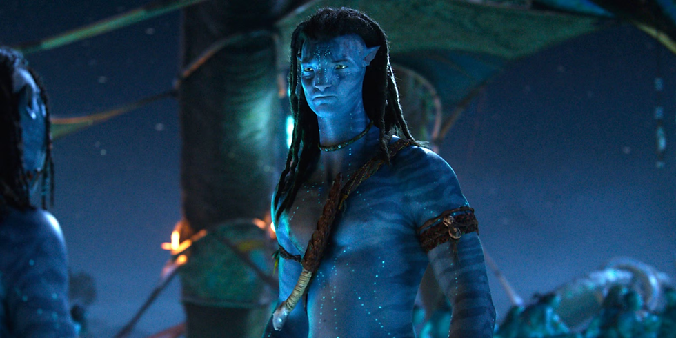 Blue humanoid figure with glowing skin stands in a dimly lit, mystical environment, wearing a necklace. The atmosphere is mysterious and calm.