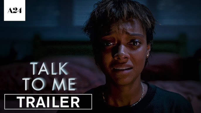 A person looks fearful in a dimly lit room; text reads "TALK TO ME TRAILER." The background is blurred, creating a tense atmosphere.