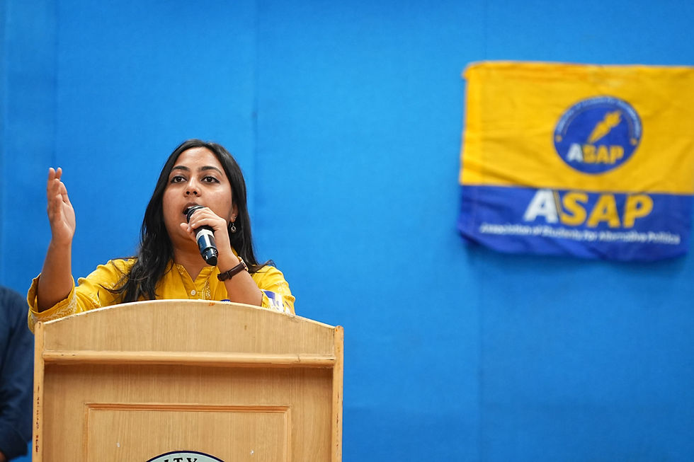 Woman in yellow speaks at a podium with a microphone, gesturing against a blue backdrop beside an ASAP/ABAP banner.