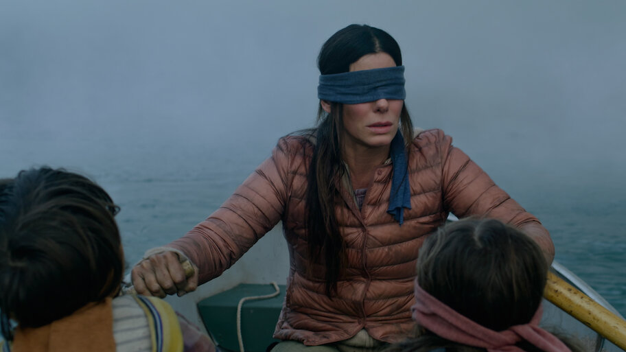 A woman with a blindfold rows a boat with two children. The scene is foggy, creating a tense, mysterious atmosphere.