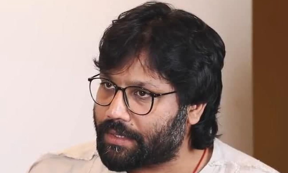 Man with glasses, beard, and long hair, wearing a light shirt, looks intently off-camera. Neutral background adds focus to expression.