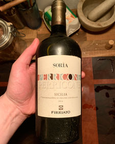 A bottle of Firriato Perricone Sicilia DOC 2016 held in hand, showing the minimalist Soria label with colored text and Sicilian origin.