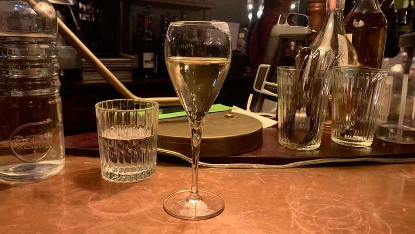 A glass of champagne on a copper countertop with an out-of-focus bar in the background.