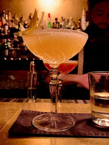Sidecar cocktail illuminated from above with beautiful bar bottles in background.