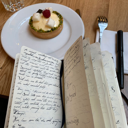 A notebook with handwritten notes in fountain pen ink, with a tarte au citron in the background, at a Parisian café