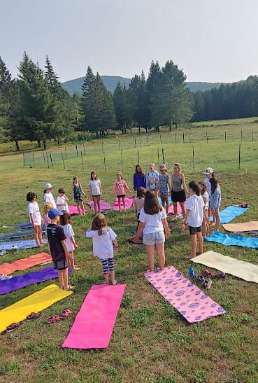 Un groupe d'enfant fait du yoga debout en rond avec des tapis au sol