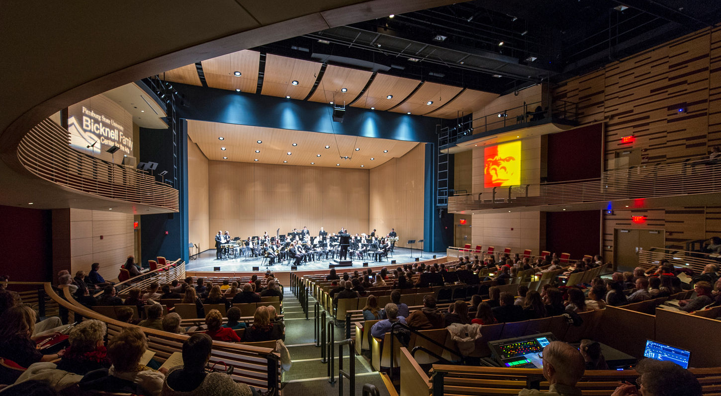 An interior view of the Mainstage Theatre at the Bicknell Family Center for the Arts. Looking from Back of House Left towards the stage. The auditorium is full, and a full orchestra is on the stage.
