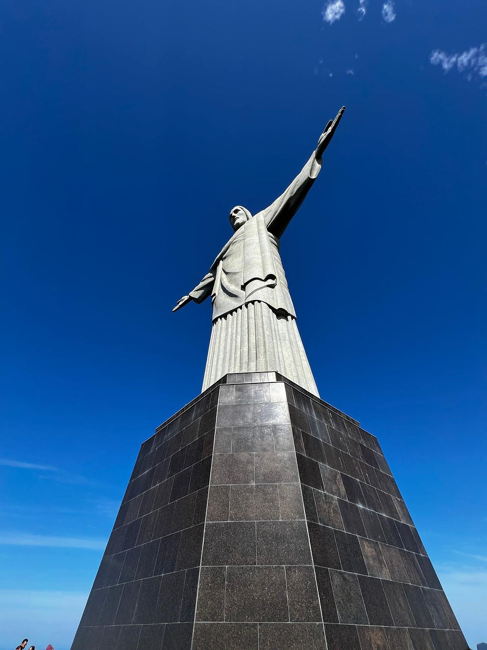 Statue of Christ the Redeemer with outstretched arms against a clear blue sky. Viewed from below, the stone structure is prominent and imposing.